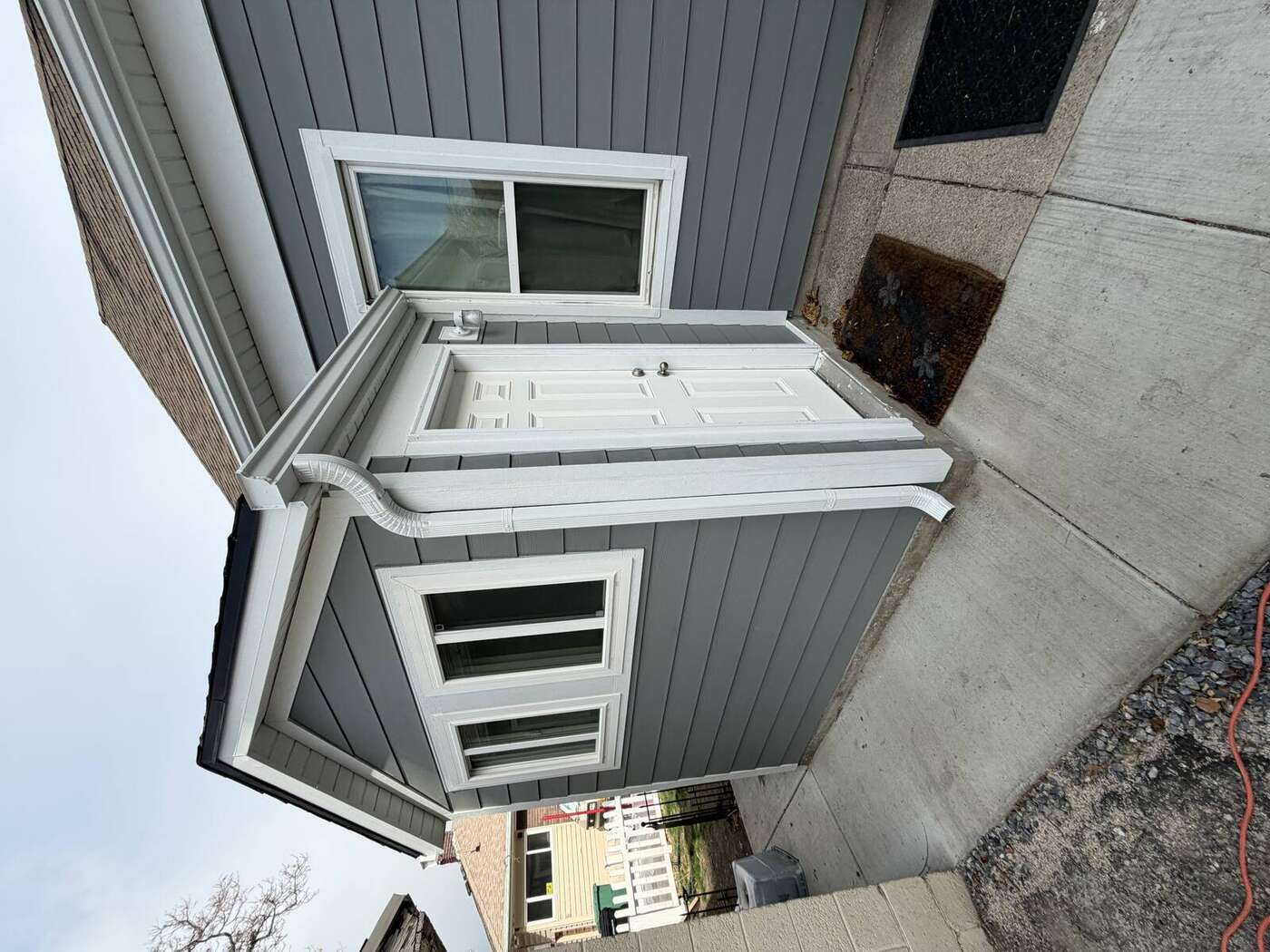 White seamless gutters with round downspout on a gray lap-siding bungalow